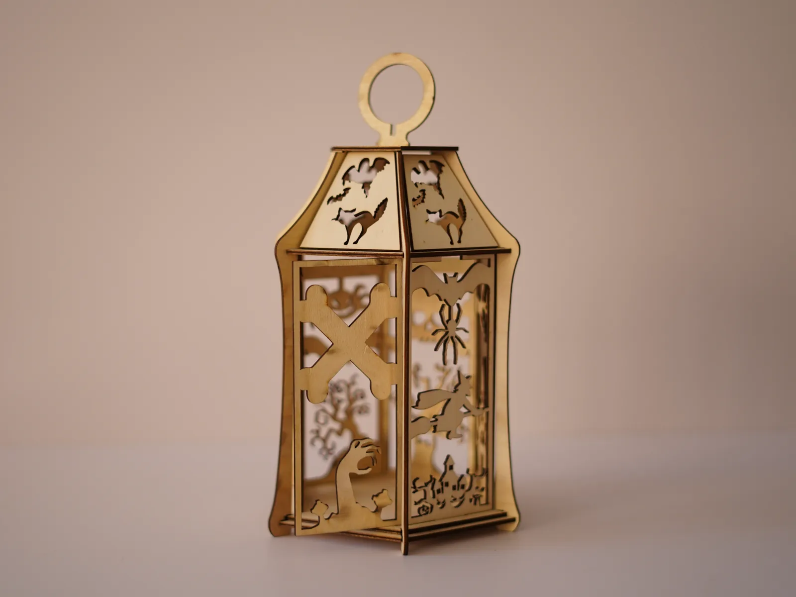An assembled laser-cut plywood Halloween lantern with bat, cat, witch and spider cutouts